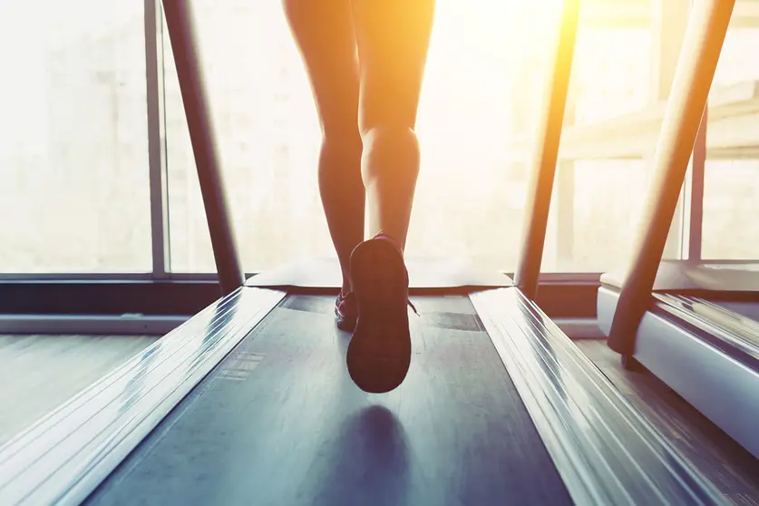 Fitness girl running on treadmill. Woman with muscular legs in gym