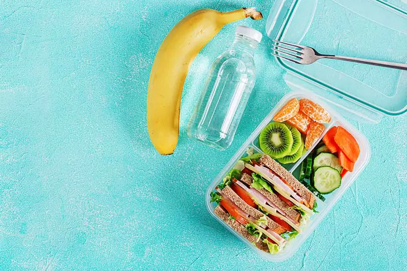 School lunch box with sandwich, vegetables, water, and fruits on table. Healthy eating habits concept. Flat lay. Top view