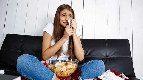 Sad young beautiful girl watching melodrama, crying, sitting on sofa at home. Copy space.